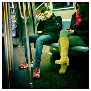 Photograph of two people sitting on the subway sharing earbuds but sitting with some distance between them