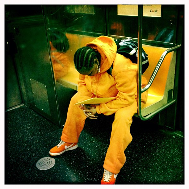 Photograph of person on subway wearing orange in orange seat